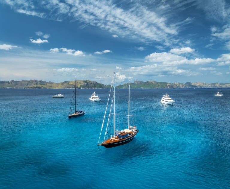 Aerial drone view of yachts and sailboats anchored in crystal clear turquoise sea near scenic coast
